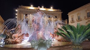 Una fuente iluminada con chorros de agua, una estatua y un edificio al fondo.
