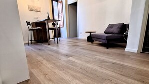 Una sala de estar moderna con piso de madera, un sofá, una mesa de comedor con sillas y una mesita con una botella.