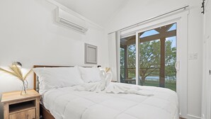 A bedroom with a large bed, a nightstand, a window with a view of trees, and a ceiling fan.
