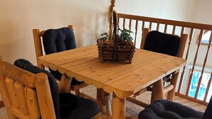 A wooden dining table with four chairs, a woven basket on the table, and a view of the outdoors through a balcony railing. - Adirondack Red House, Adirondack Red House (Eagle Bay)