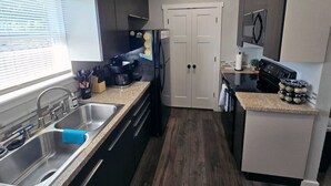 A compact kitchen with dark cabinets, a stainless steel sink, a black refrigerator, and a countertop with a coffee maker and jars.