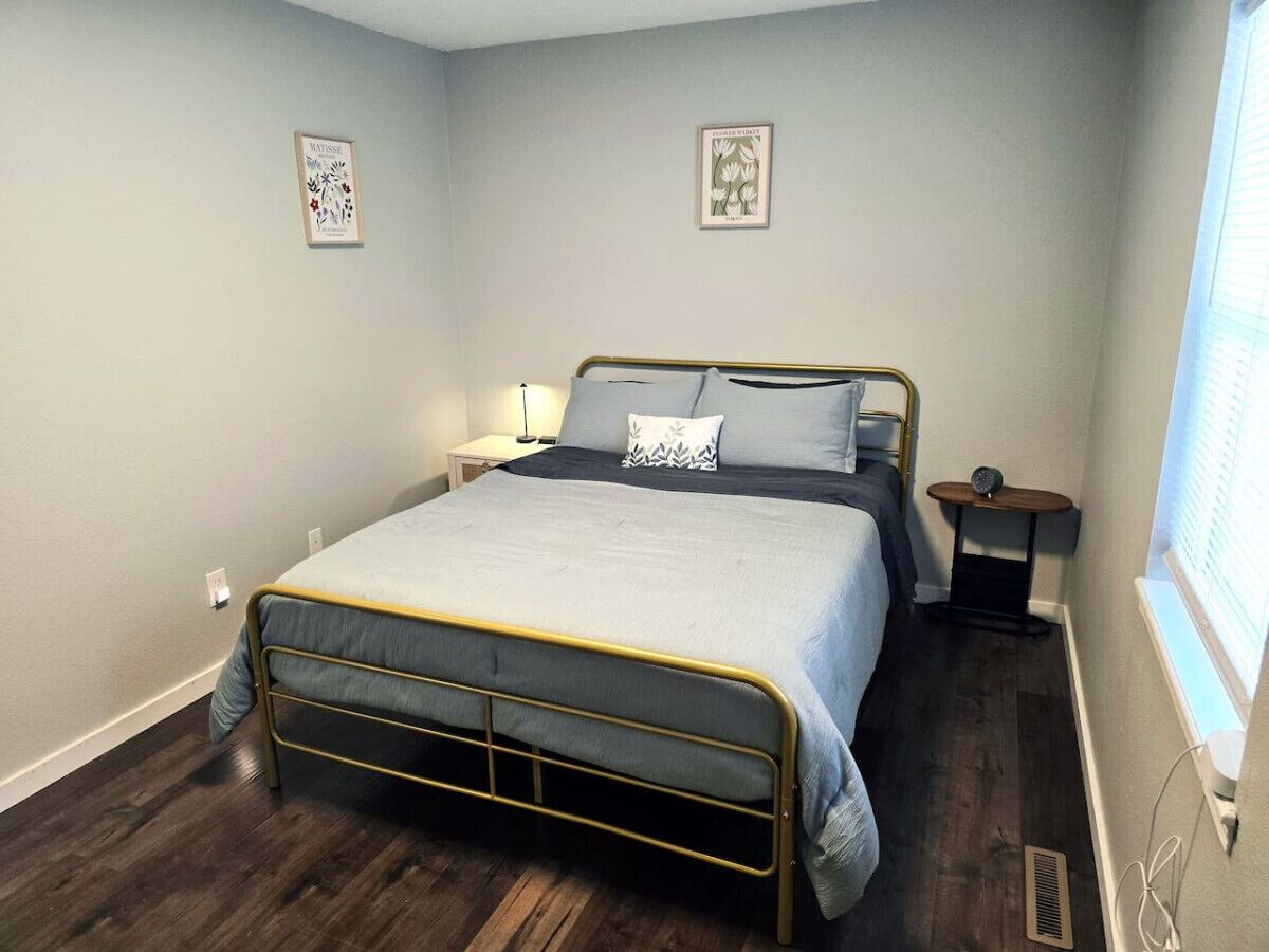 A bedroom with a bed, a bedside table, a nightstand, a window, and two wall art pieces.
