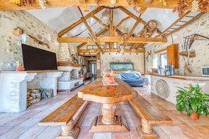 Un interior rústico con una mesa de comedor de madera, paredes de piedra y un techo alto con vigas a la vista.