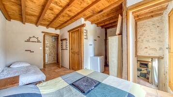 A bedroom with a bed, a small desk, a refrigerator, and a wooden ceiling.