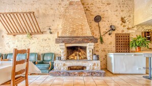A rustic interior with a stone fireplace, green leather seating, and a white refrigerator. - Holiday Home 'La Grange' with Private Pool, Private Terrace and Wi-Fi (Guizengeard)