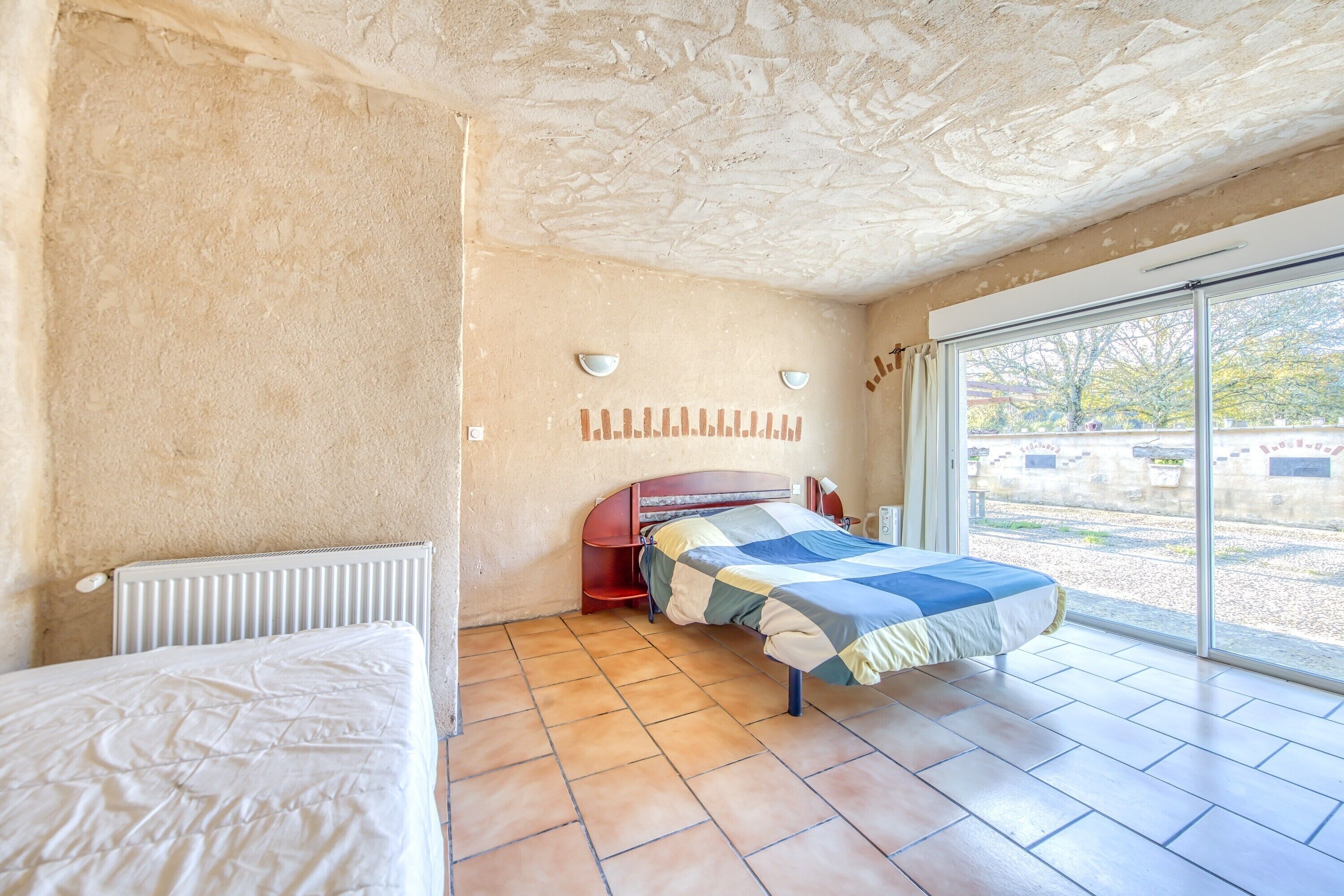 Une chambre à coucher avec un lit, un radiateur, une fenêtre et une vue sur l’extérieur.