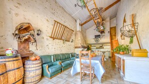 A rustic interior with a green leather sofa, wooden barrels, a dining table with a white tablecloth, and a wooden ladder. - Holiday Home 'La Grange' with Private Pool, Private Terrace and Wi-Fi (Guizengeard)