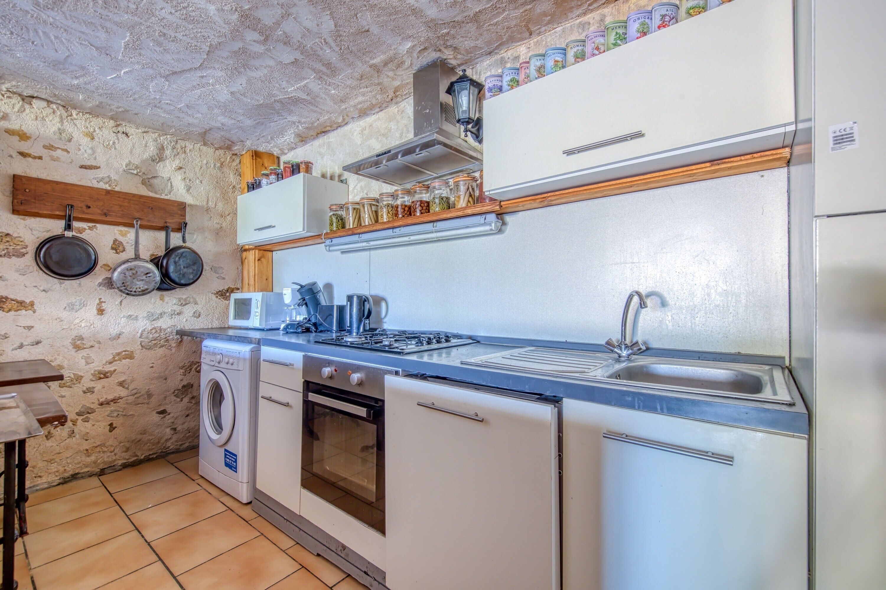 Cocina compacta con lavadora, estufa, lavaplatos y ollas colgantes.