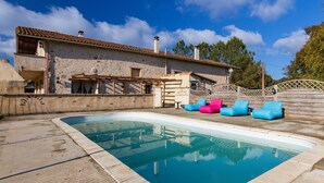 A swimming pool with a stone wall, a wooden deck, and outdoor seating. - Holiday Home 'L'Ecurie' with Private Pool, Private Terrace and Wi-Fi (Guizengeard)