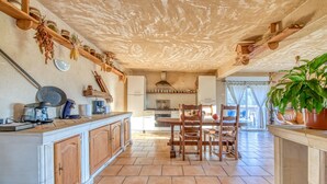 A spacious kitchen with wooden cabinets, a dining area with chairs, a large potted plant, and a view of the living area. - Holiday Home 'L'Ecurie' with Private Pool, Private Terrace and Wi-Fi (Guizengeard)