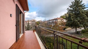 Un balcón con barandilla metálica, una pared rosa y vistas a una zona residencial con árboles y edificios.