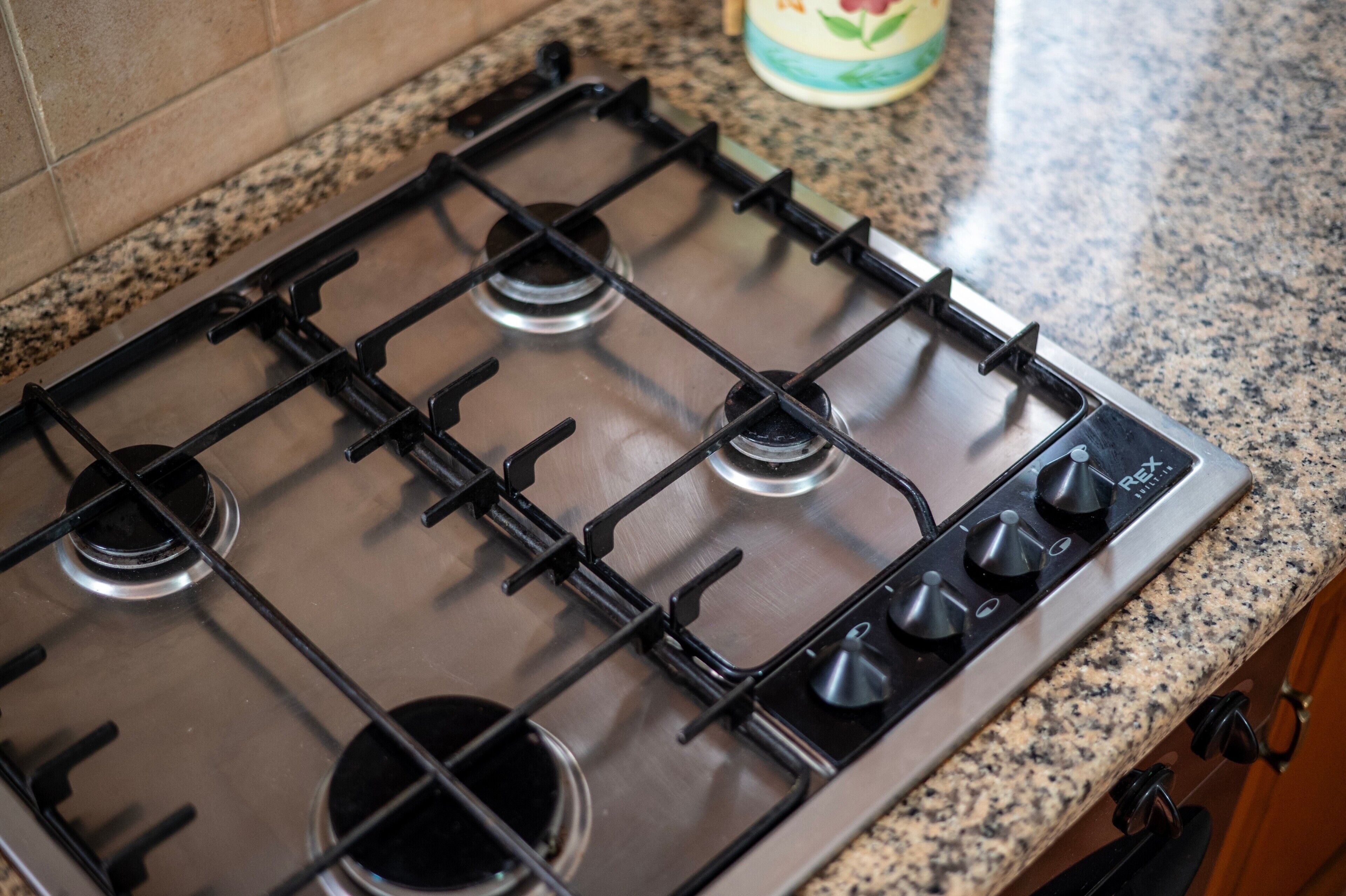 Une cuisine équipée d’une cuisinière à gaz en acier inoxydable, d’un plan de travail en granit et de meubles de rangement en bois.