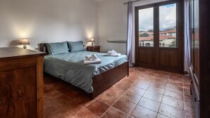 Un dormitorio con una cama, dos mesitas de noche con lámparas, un aparador de madera y vistas a través de un ventanal grande.