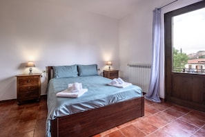 A bedroom with a wooden bed, two bedside tables, a window with a view, and a radiator. - Apartment 'Casa Doriana' with Balcony and Wi-Fi (Poggio Murella)
