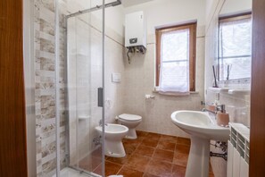 A bathroom with a glass shower enclosure, two toilets, a sink, and a window.