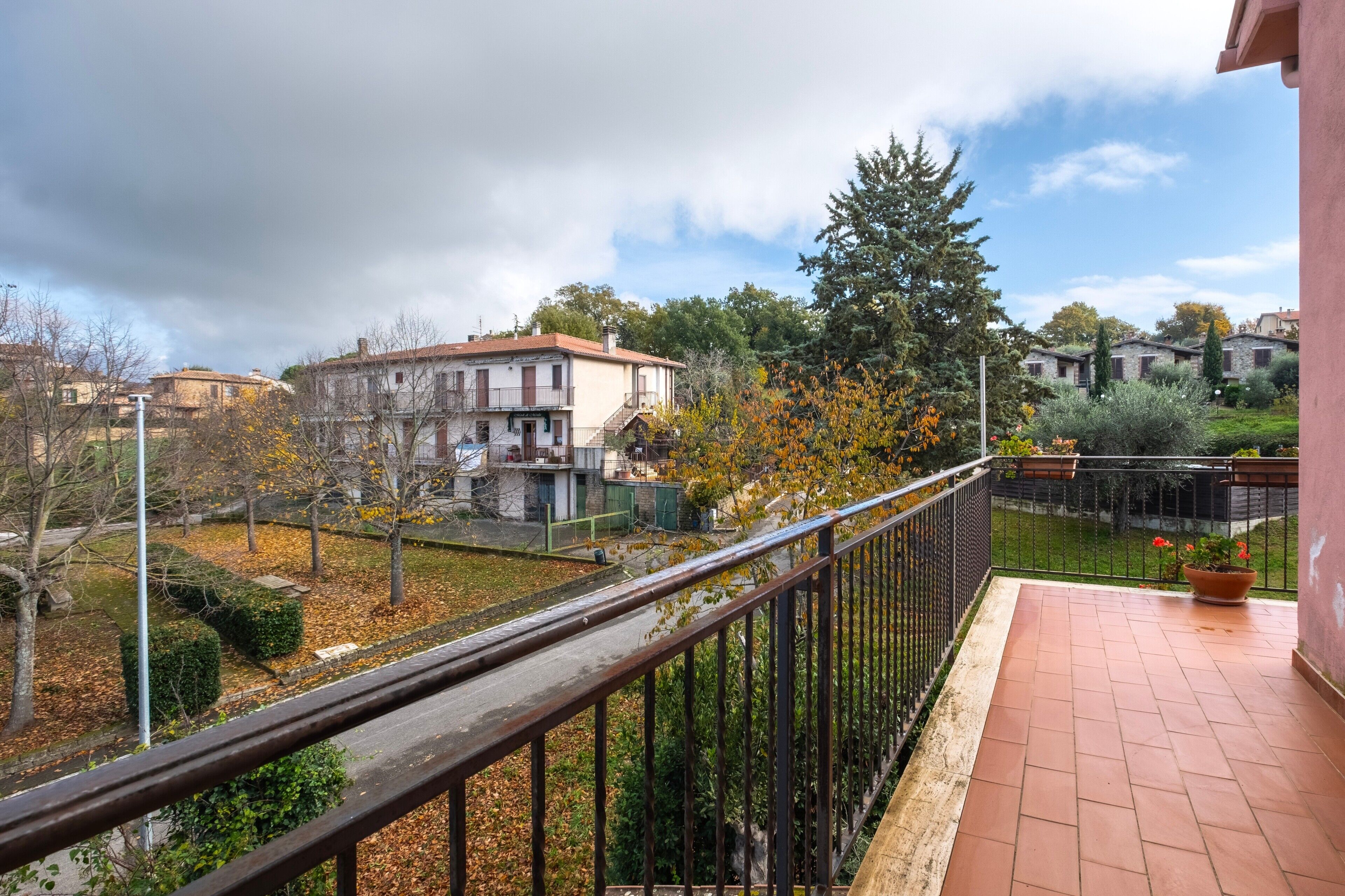 A balcony with a metal railing, a tiled floor, and a view of a residential area with houses and trees.