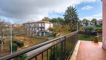A balcony with a metal railing, a tiled floor, and a view of a residential area with houses and trees.
