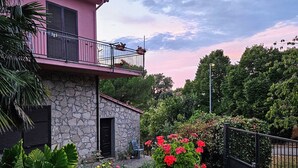 Una casa con balcón, paredes de piedra y un jardín lleno de flores.