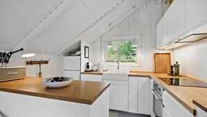 Une cuisine moderne avec des meubles blancs, un plan de travail en bois, une fenêtre donnant sur un paysage verdoyant et une radio Marshall vintage.