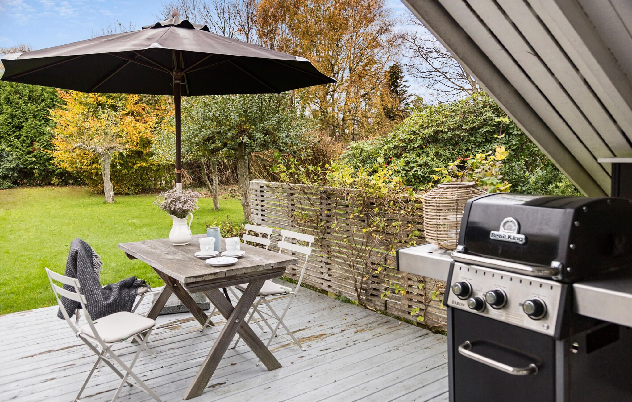 An outdoor patio with a wooden table, chairs, a grill, and an umbrella.