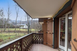 A wooden balcony with a tiled floor, a glass door, and a view of a rural landscape.