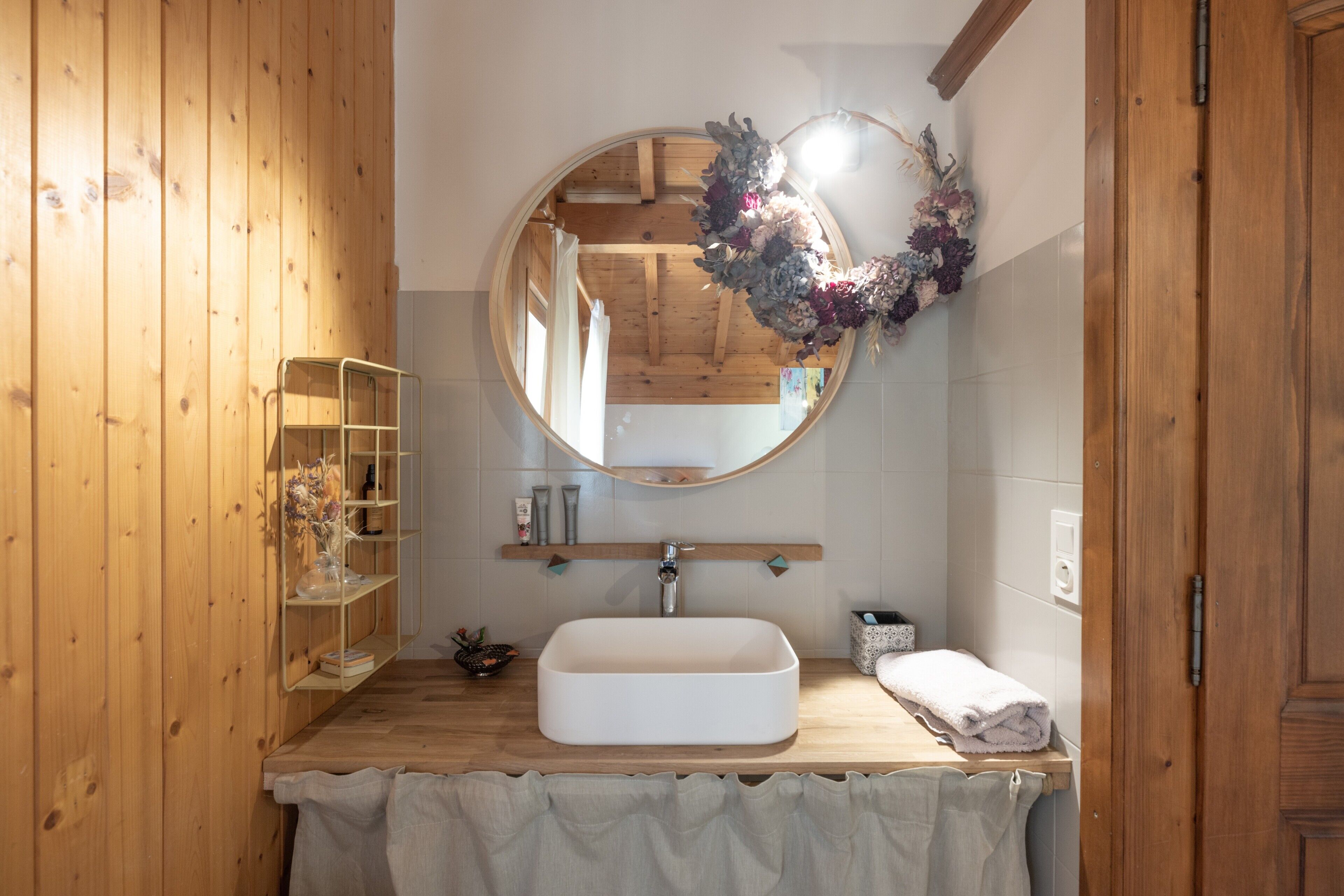 A bathroom with a wooden vanity, a round mirror, a white sink, and a towel rack.