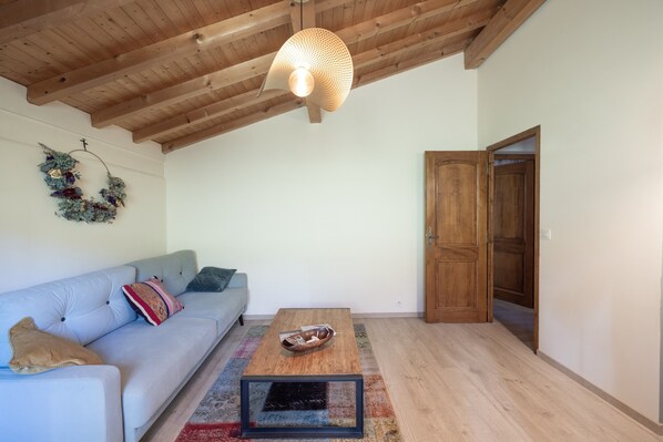 Una sala de estar con un sofá, una mesa de centro, techo de madera y una puerta.