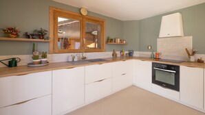 Een moderne keuken met witte kasten, een houten aanrechtblad, een dubbele spoelbak en een inbouwoven.