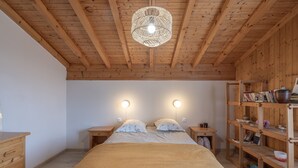 Een slaapkamer met een houten plafond, een bed met een beige deken, nachtkastjes met lampen en een houten boekenkast.