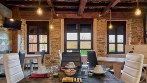 A dining area with a table set for two, stone walls, wooden ceiling beams, and a view through the windows.