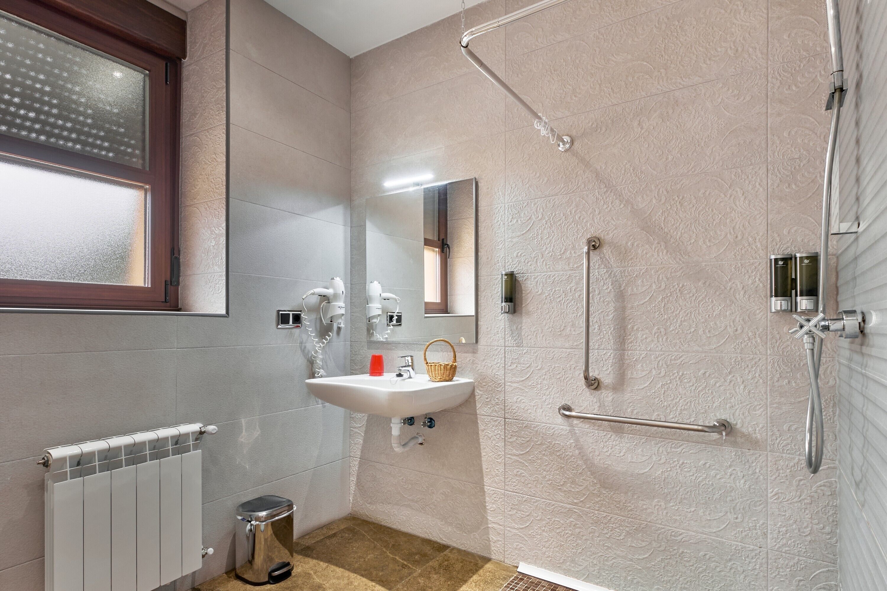 Un baño con ducha, lavabo, espejo, radiador y ventana.