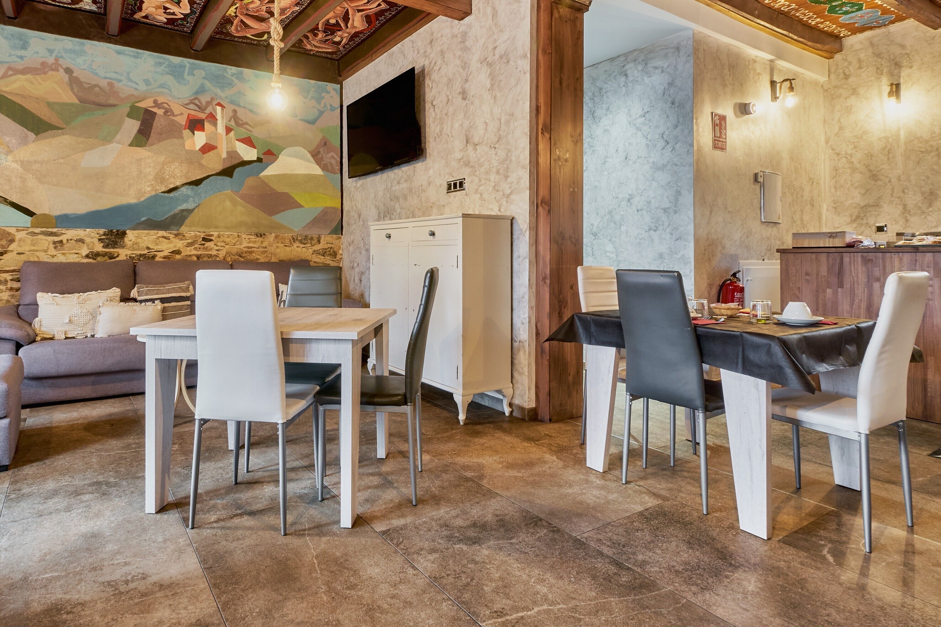 Un comedor con una mesa, sillas, un sofá, un televisor y un mural en la pared.