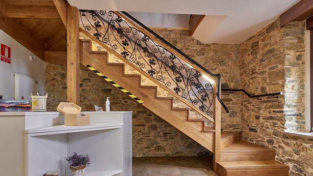 A wooden staircase with a wrought iron railing, stone walls, and a white shelving unit with decorative items.