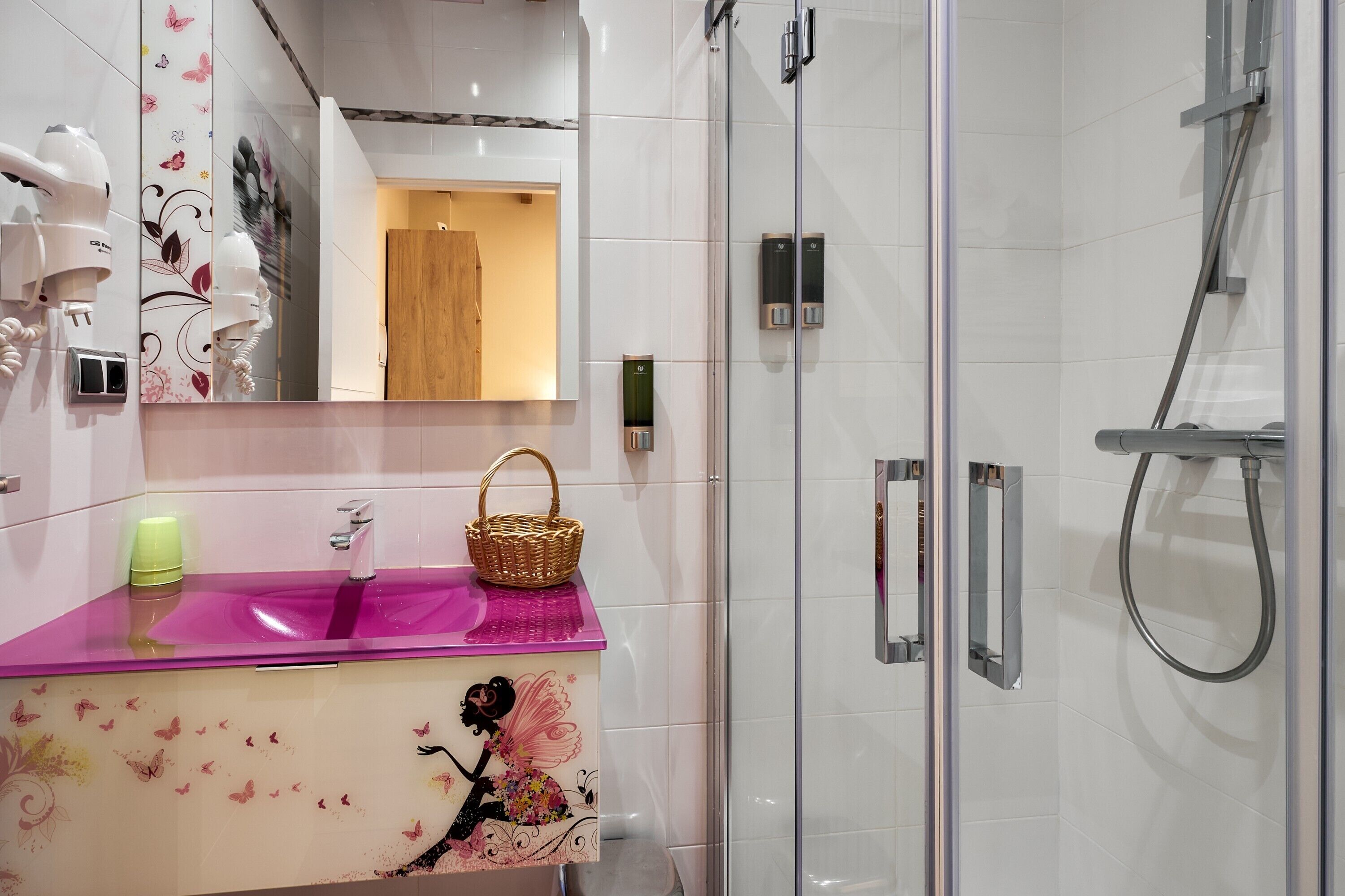 Een badkamer met een roze wastafel, een spiegel, een douche en een opbergwand gemonteerde haardroger.