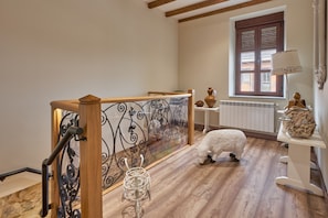 Un escalier en bois avec une rampe en métal, une sculpture de mouton blanc et une fenêtre avec des volets.
