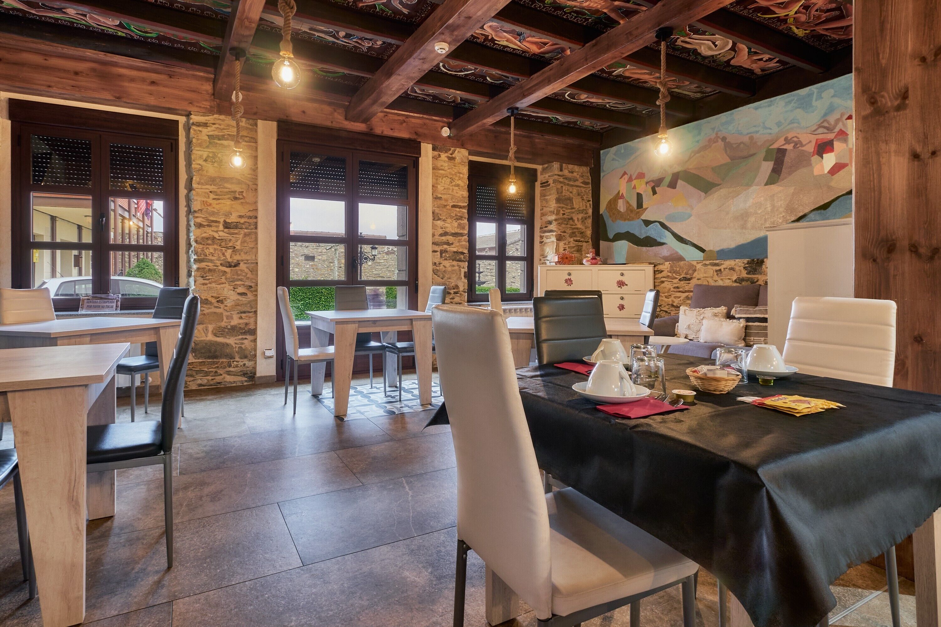 A dining area with a table set for four, stone walls, wooden beams, and a mural on the wall.