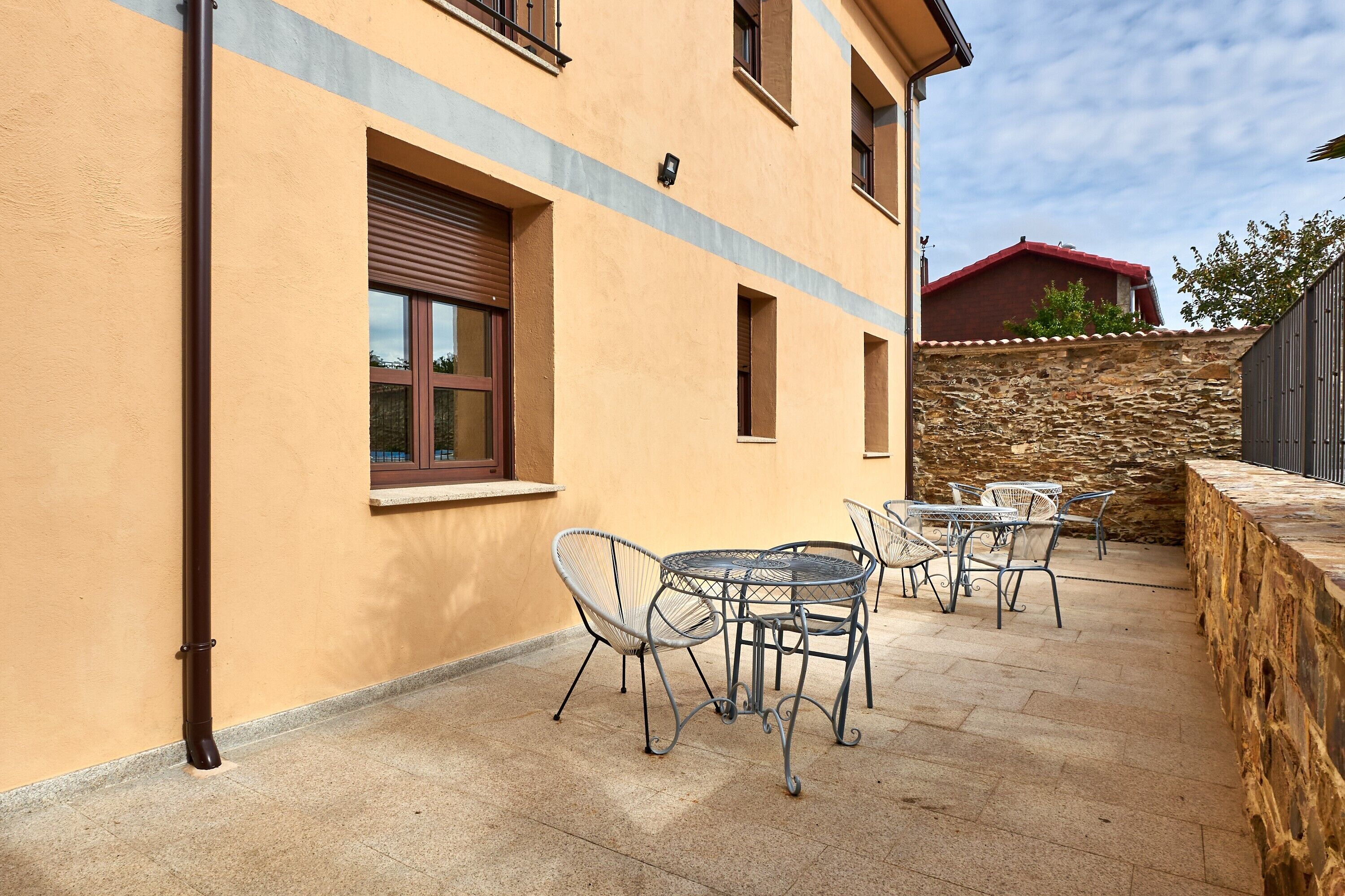 A building with a yellow exterior, a stone wall, and a patio with metal chairs and a table.