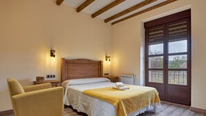 Un dormitorio con una cama, una silla, cabecero de madera, dos lámparas de noche, una ventana con vistas y un radiador.