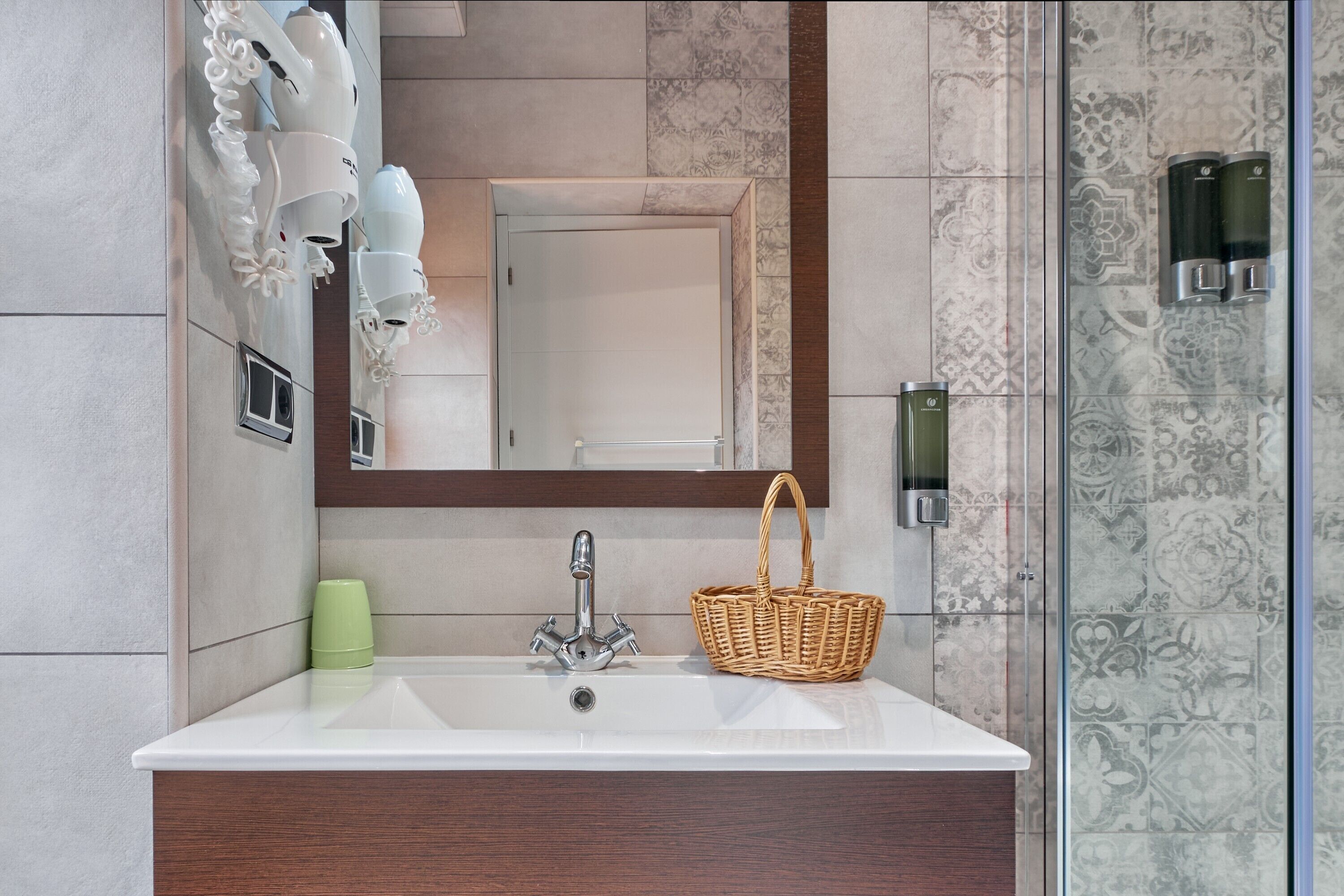 A bathroom with a white sink, a mirror, a shower, and a wicker basket.