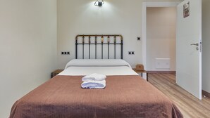 Una cama bien hecha con una colcha marrón, una lámpara arriba y una puerta a la derecha.
