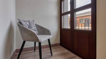 Habitación de esquina con una silla, piso de madera, ventana con vista a un edificio y puerta de madera.
