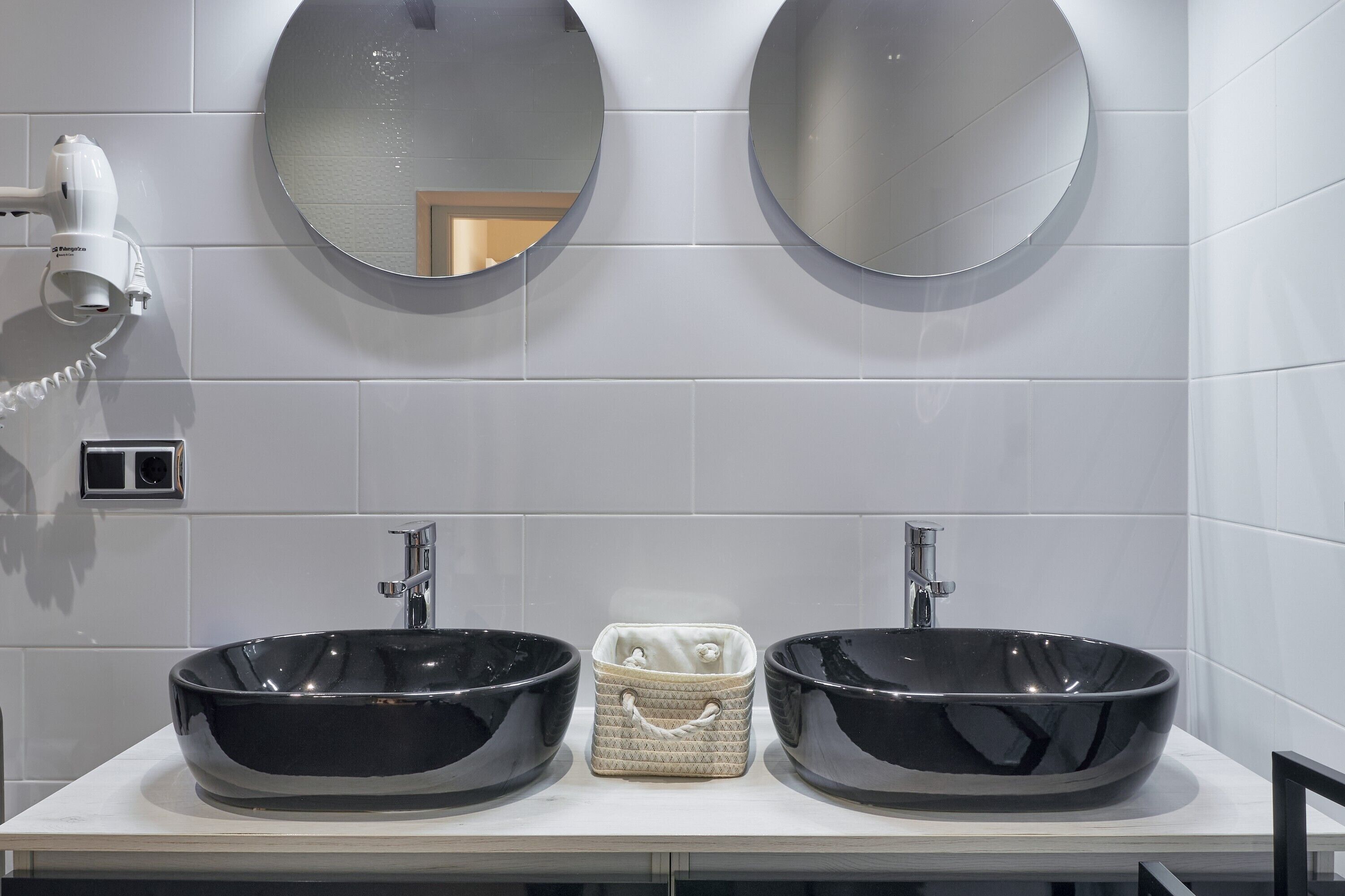 A bathroom with two black sinks, a hairdryer, and a mirror.