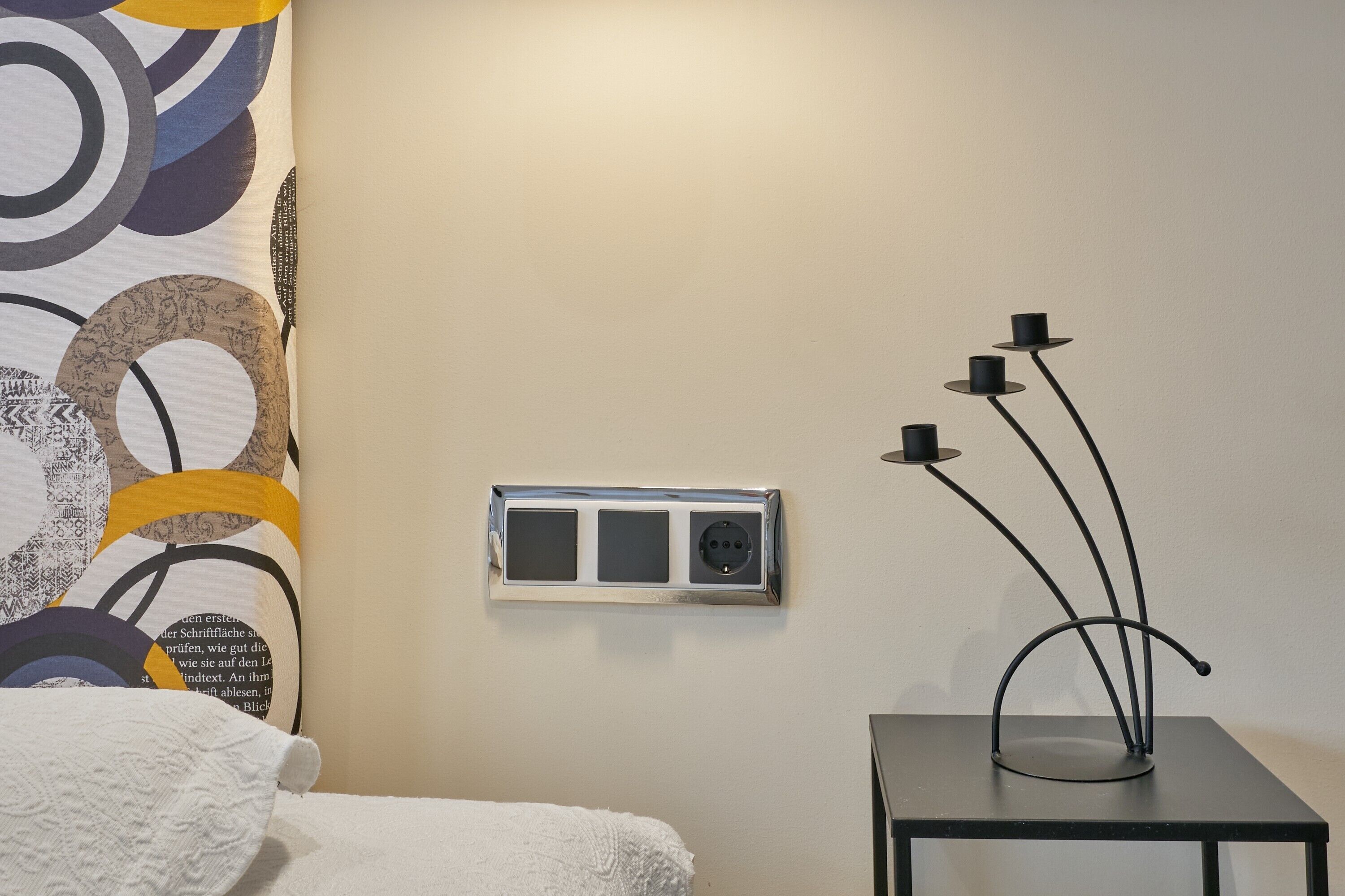 Una habitación de hotel con una cama, un enchufe en la pared y una escultura decorativa de metal negro.