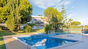 A swimming pool with a tiled deck, surrounded by trees and a building in the background. - Apartment 'Casa Oliveira - Algarve' with Sea View, Wi-Fi and Air Conditioning (Porches)