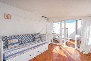 Habitación con sofá blanco, cama blanca, balcón con mesa y sillas, y vista al cielo.