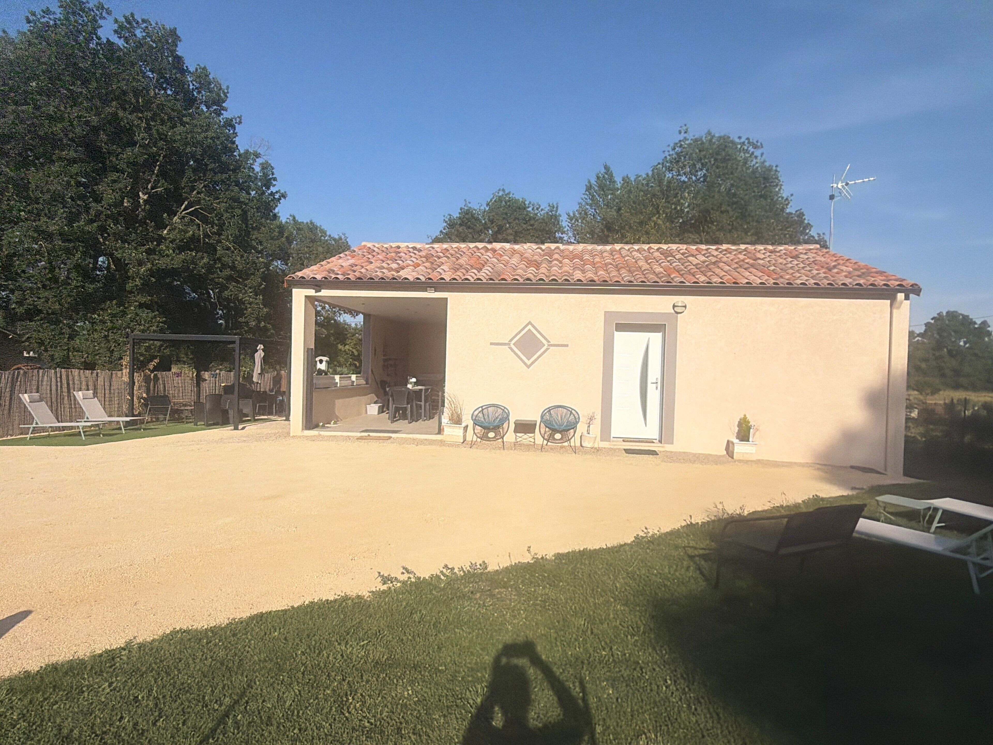 Un petit bâtiment doté d’un toit en tuiles, d’une porte et d’un espace extérieur abrité, aménagé avec des chaises et des tables.