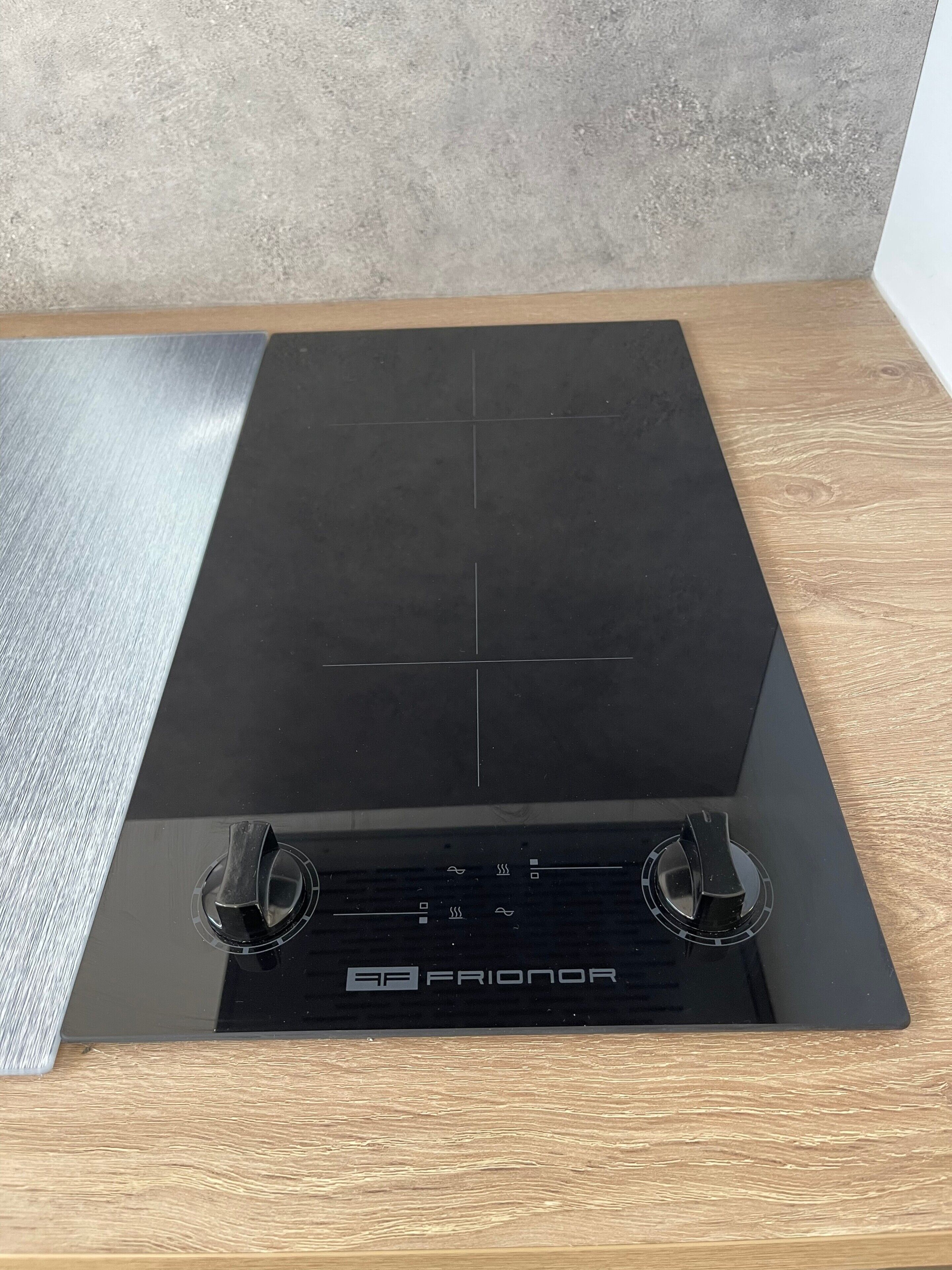 A black induction cooktop with control knobs and a digital display, set on a wooden countertop against a concrete wall.