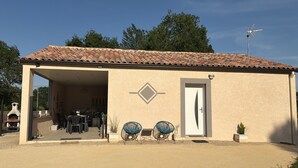 Un bâtiment doté d’un toit en tuiles, d’une porte et d’un petit jardin avec deux chaises et une plante en pot.