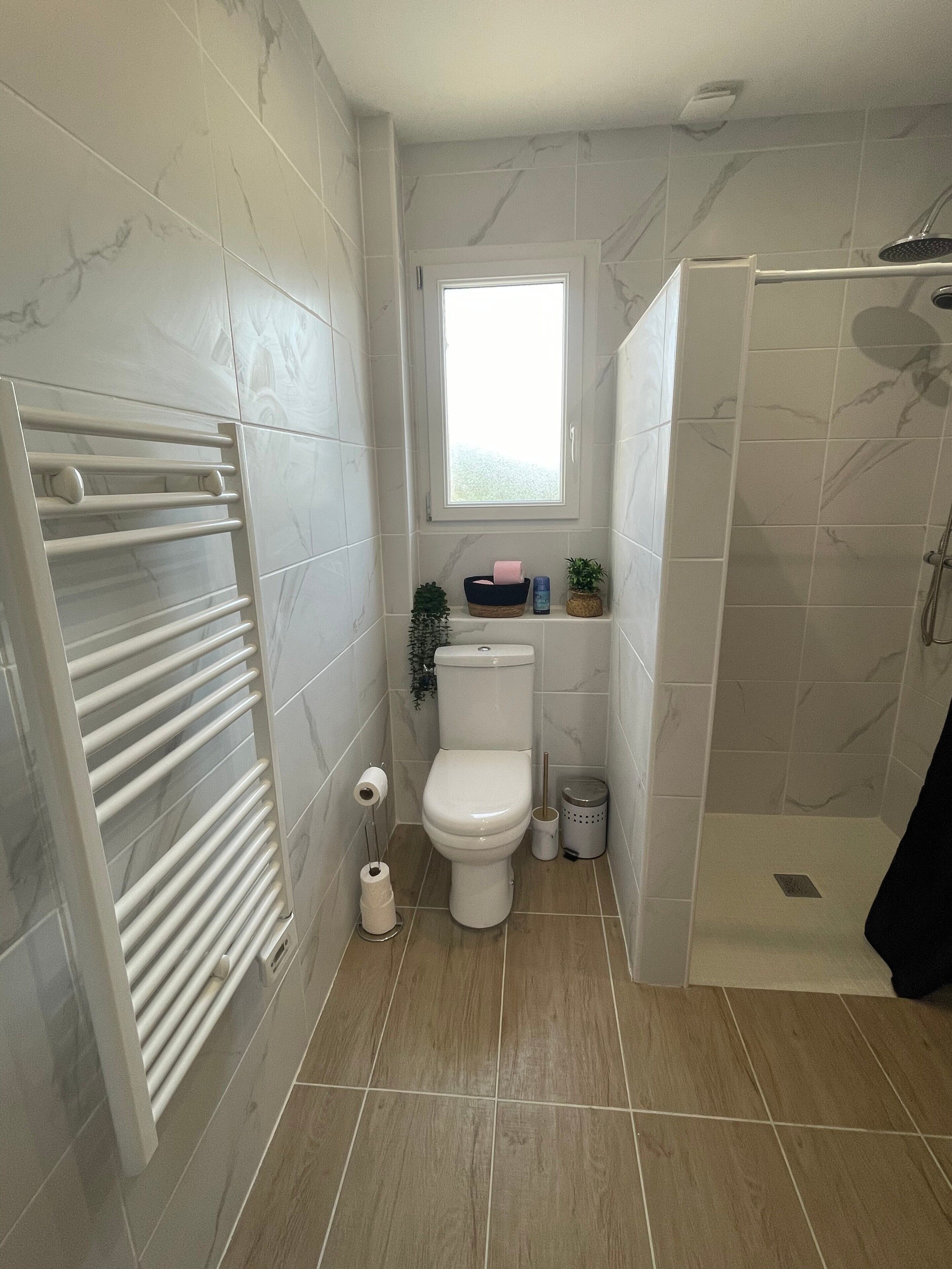 Une salle de bain comprenant des toilettes, un bidet, une douche et une fenêtre.
