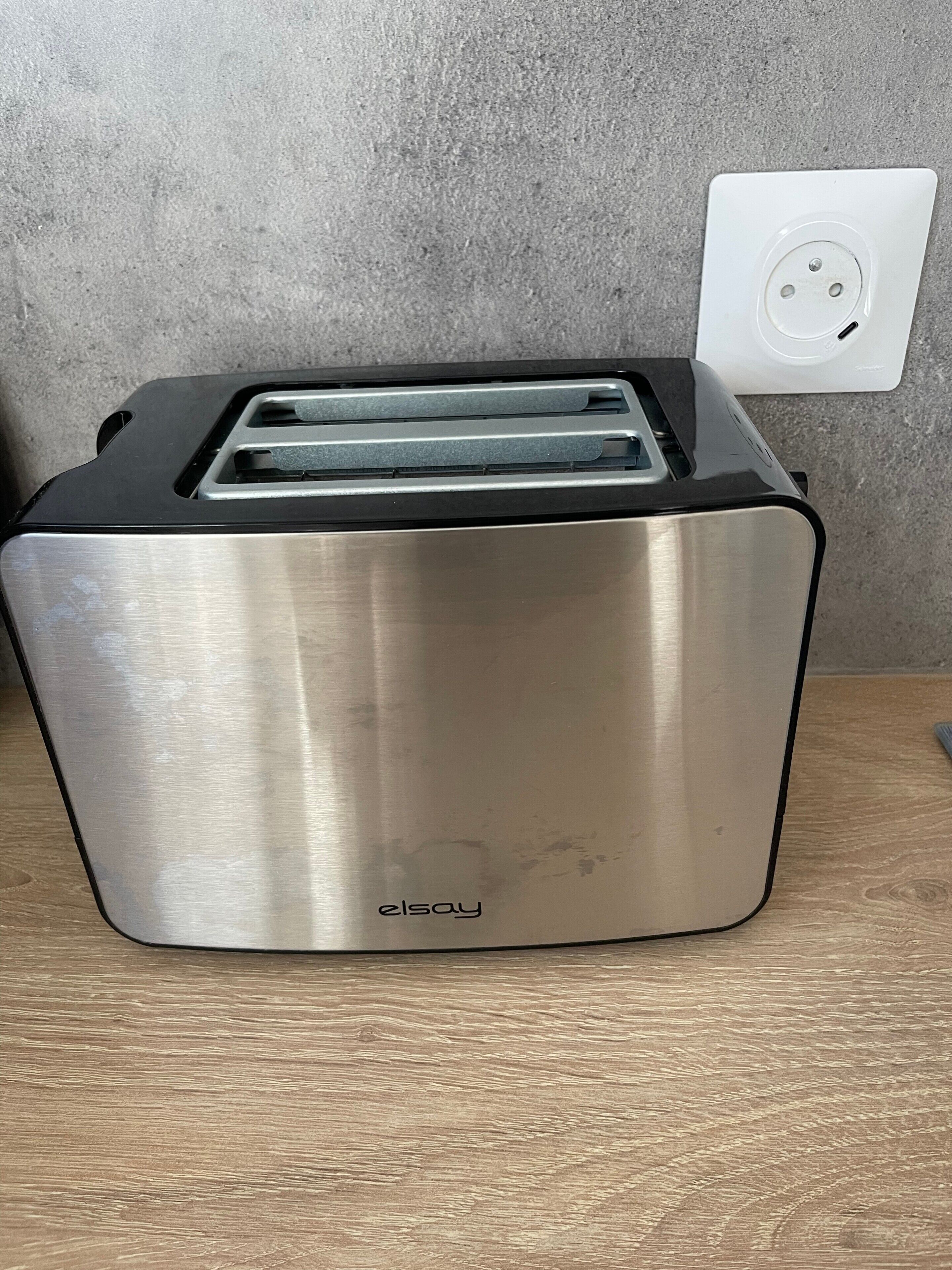 A stainless steel toaster with a black top, placed on a wooden surface.